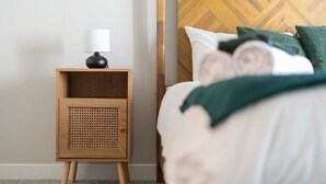 A neatly made bed with green and white bedding, a wooden nightstand with a lamp, and a headboard with a herringbone pattern. - Charming Tempe 1BR Designer Furnishings, Patio & Gym (Tempe)