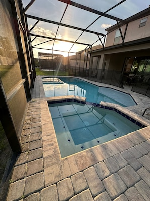 A swimming pool with a glass enclosure, surrounded by a patio area with stone tiles.