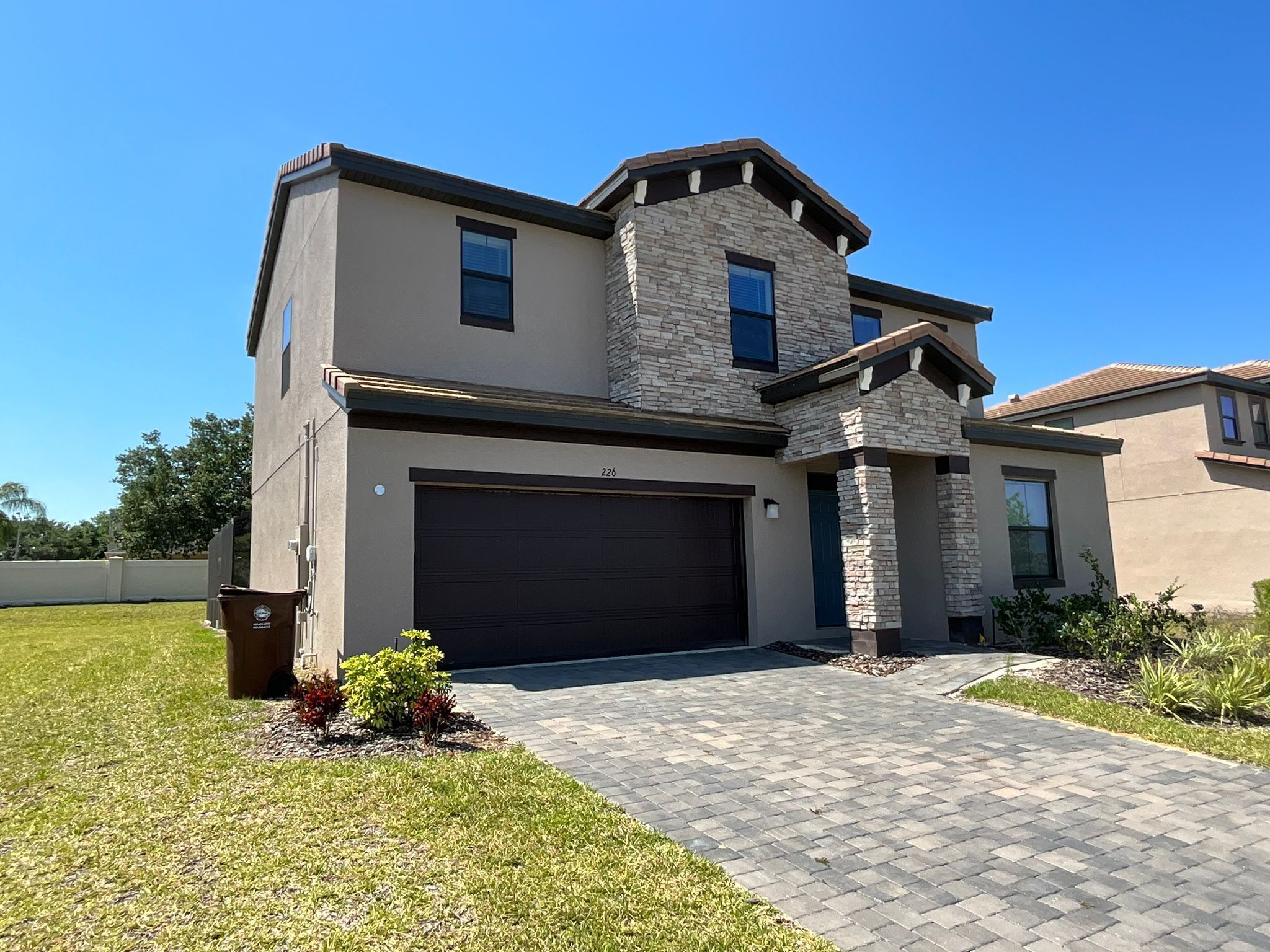 A modern two-story house with a stone facade, a garage, and a well-maintained lawn.
