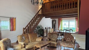 A spacious living room with a high wooden ceiling, a staircase, leather sofas, a patterned armchair, and a dining table with chairs. - Lovely, cosy villa in the Cévennes (Chamborigaud)