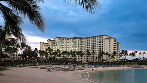 A beachfront hotel with multiple floors, palm trees, and a sandy beach.