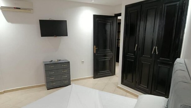 A bedroom with a bed, a dresser, a TV, and dark wooden wardrobes. - holidaysapparte-marrakech (Marrakech)