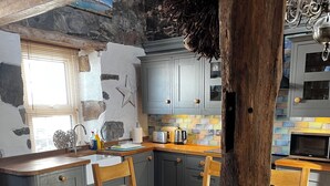 A rustic kitchen with wooden cabinets, a dining table with chairs, and a stone wall. - Fantastic 1-bedroom house in Portpatrick (Portpatrick)