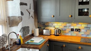 A kitchen with a stone wall, wooden countertop, and grey cabinets. - Fantastic 1-bedroom house in Portpatrick (Portpatrick)
