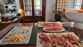 Uma mesa de jantar com jogos americanos de jornal, uma máquina de café e uma seleção de carnes e queijos.