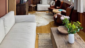 A room with a large window, a round ceiling light, a sofa, a chair, a small table, and a vase with flowers. - Hotel Quinta Solera (Oviedo)