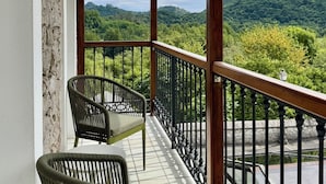A balcony with wicker chairs, a wooden railing, and a view of green hills. - Hotel Quinta Solera (Oviedo)