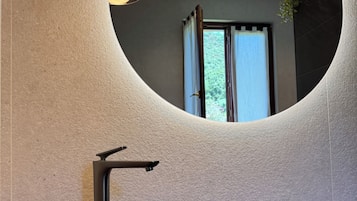 Une salle de bain moderne avec un miroir rond, un lavabo noir et une plante suspendue.