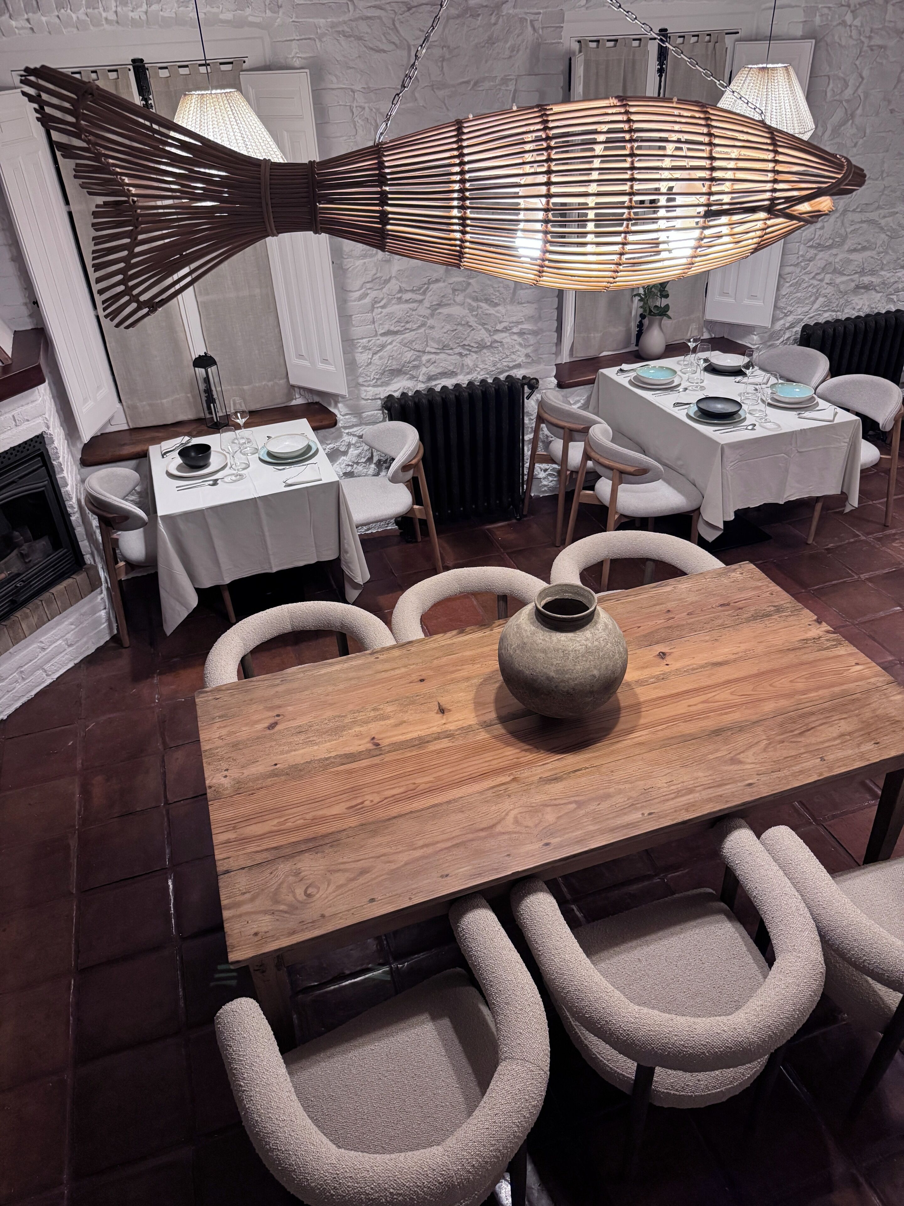A dining area with a wooden table, four chairs, a vase, and a hanging light fixture.