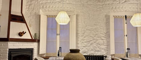 Et rustikt interiør med synlige træbjælker, en stenvæg, en pejs og to hængende lamper.