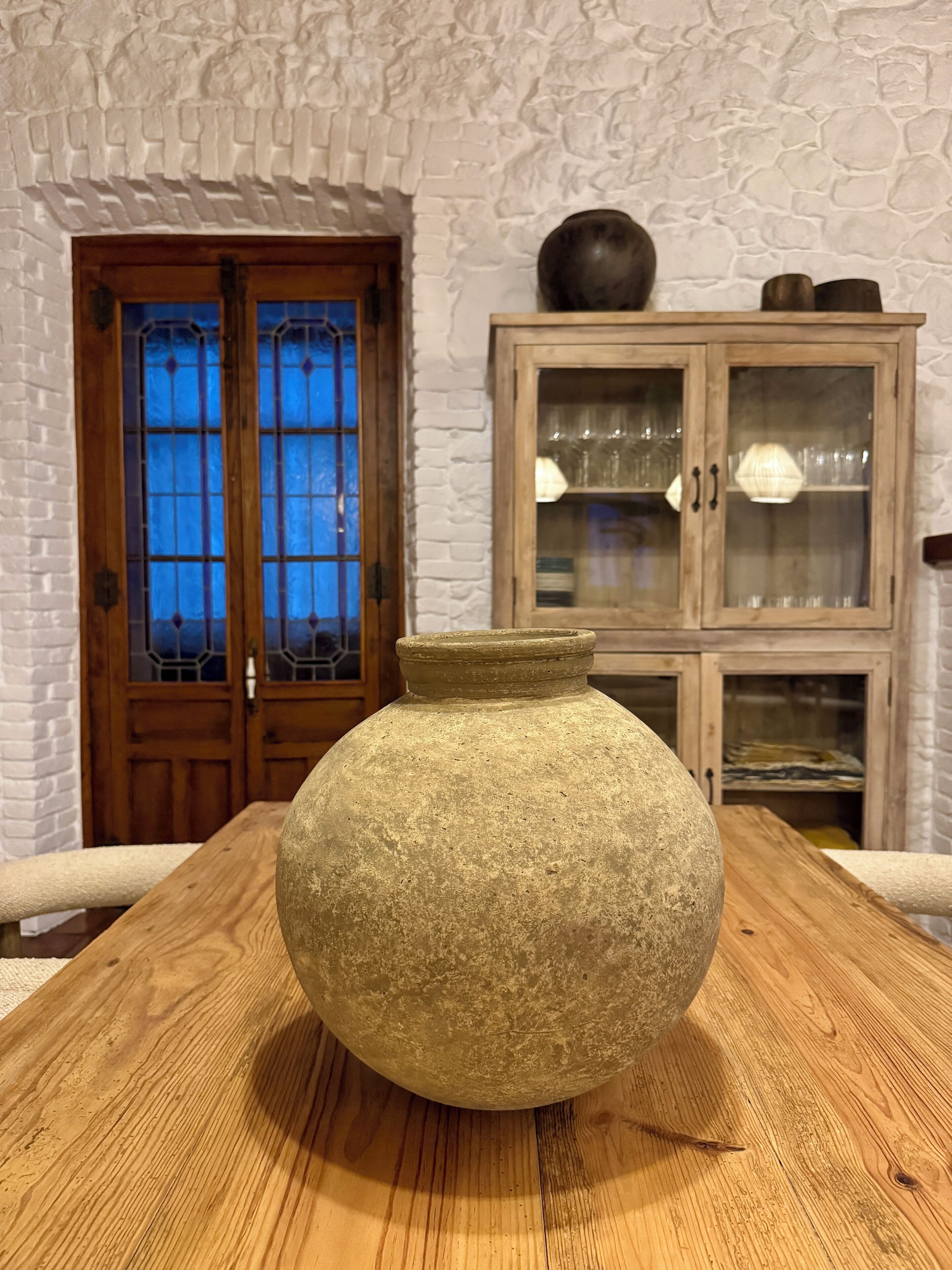 A stone vase on a wooden table in a room with a stone wall and wooden door.
