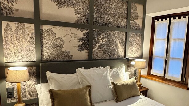 A neatly made bed with white linens and two pillows, a quilted blanket, and a folded robe on the bed. There are two bedside lamps on wooden nightstands. - Hotel Quinta Solera (Oviedo)