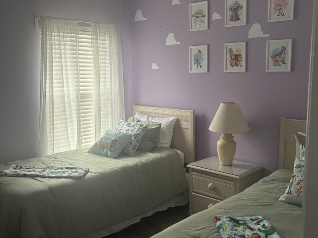 A bedroom with two beds, a nightstand, a lamp, and a window with blinds.
