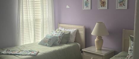 A bedroom with two beds, a nightstand, a lamp, and a window with blinds.