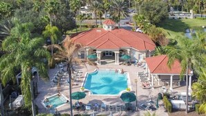 Un resort con piscina central, zonas de descanso y palmeras.