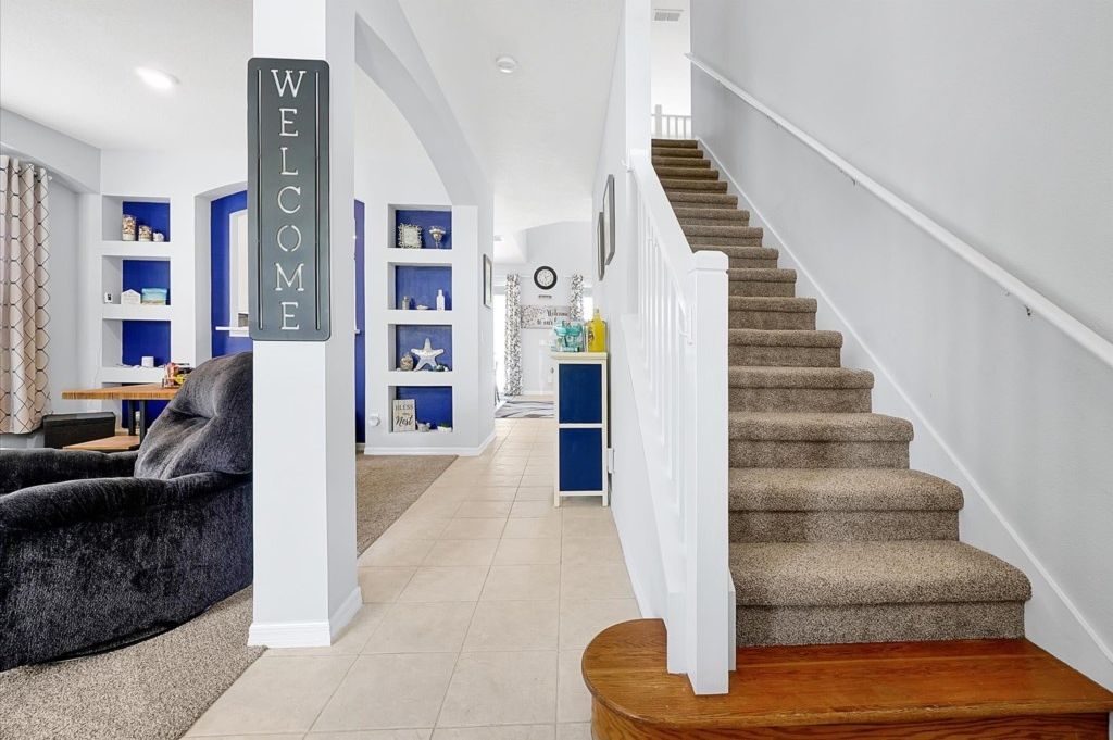 Una sala de estar moderna con un sofá gris, una escalera con peldaños cubiertos de alfombra beige y estanterías azules.