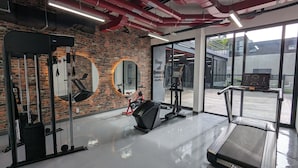 Un gimnasio con equipo de ejercicio, una pared de ladrillo y amplios ventanales.
