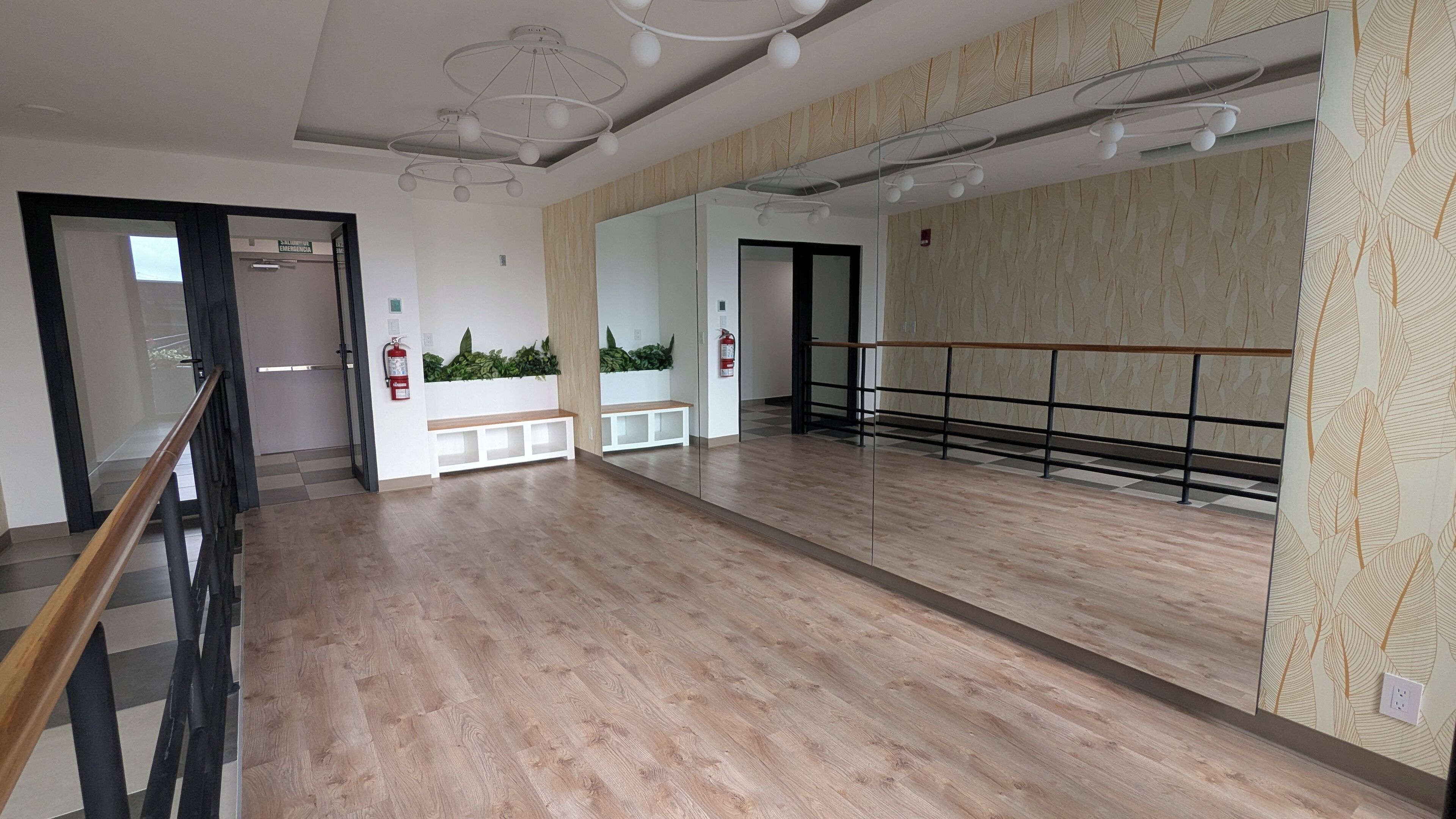 Une pièce spacieuse avec un grand miroir, un plancher en bois, un banc et une barre de ballet.
