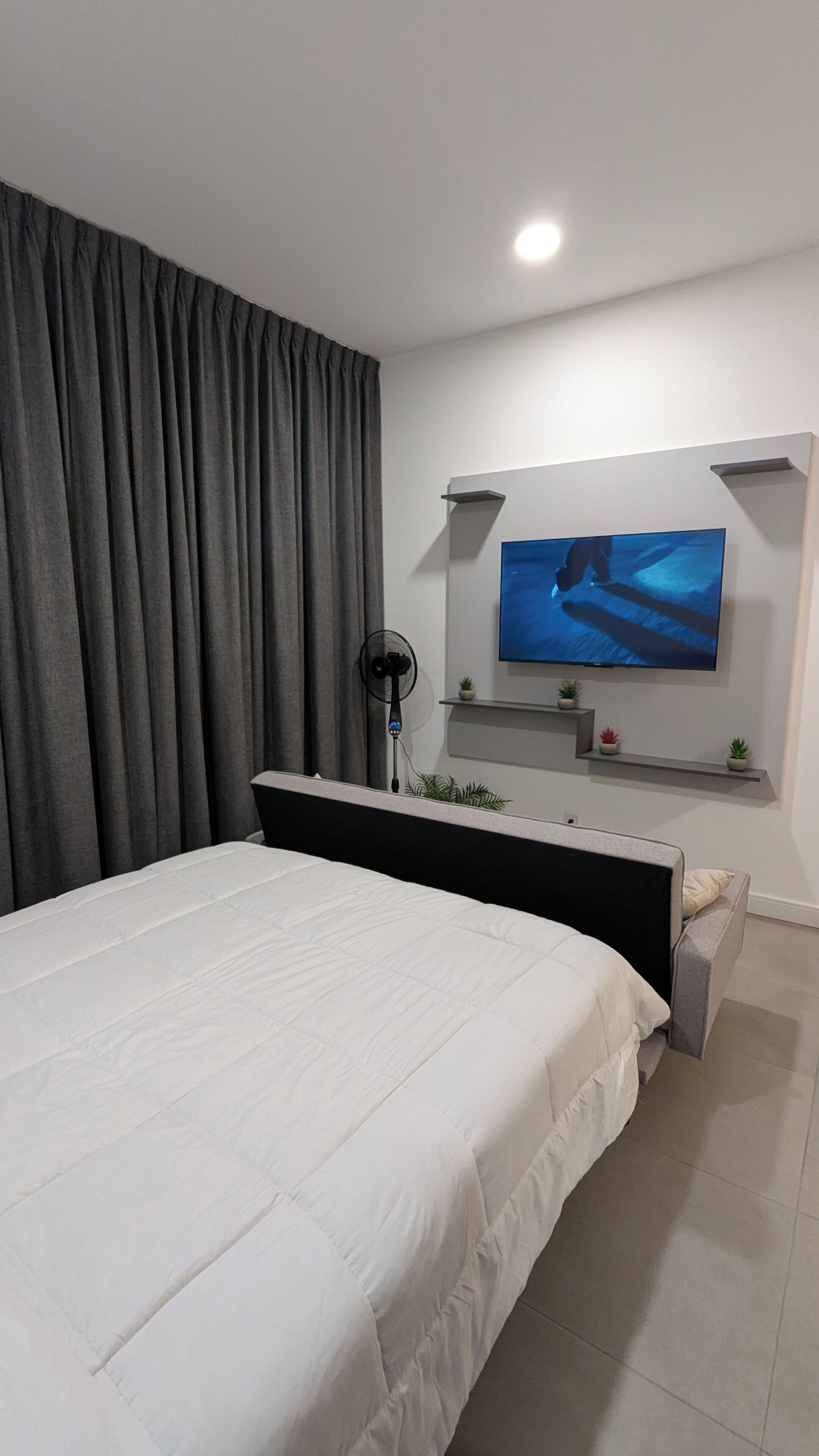 Un dormitorio moderno con una cama grande, un televisor de pantalla plana en la pared y un estante con plantas.