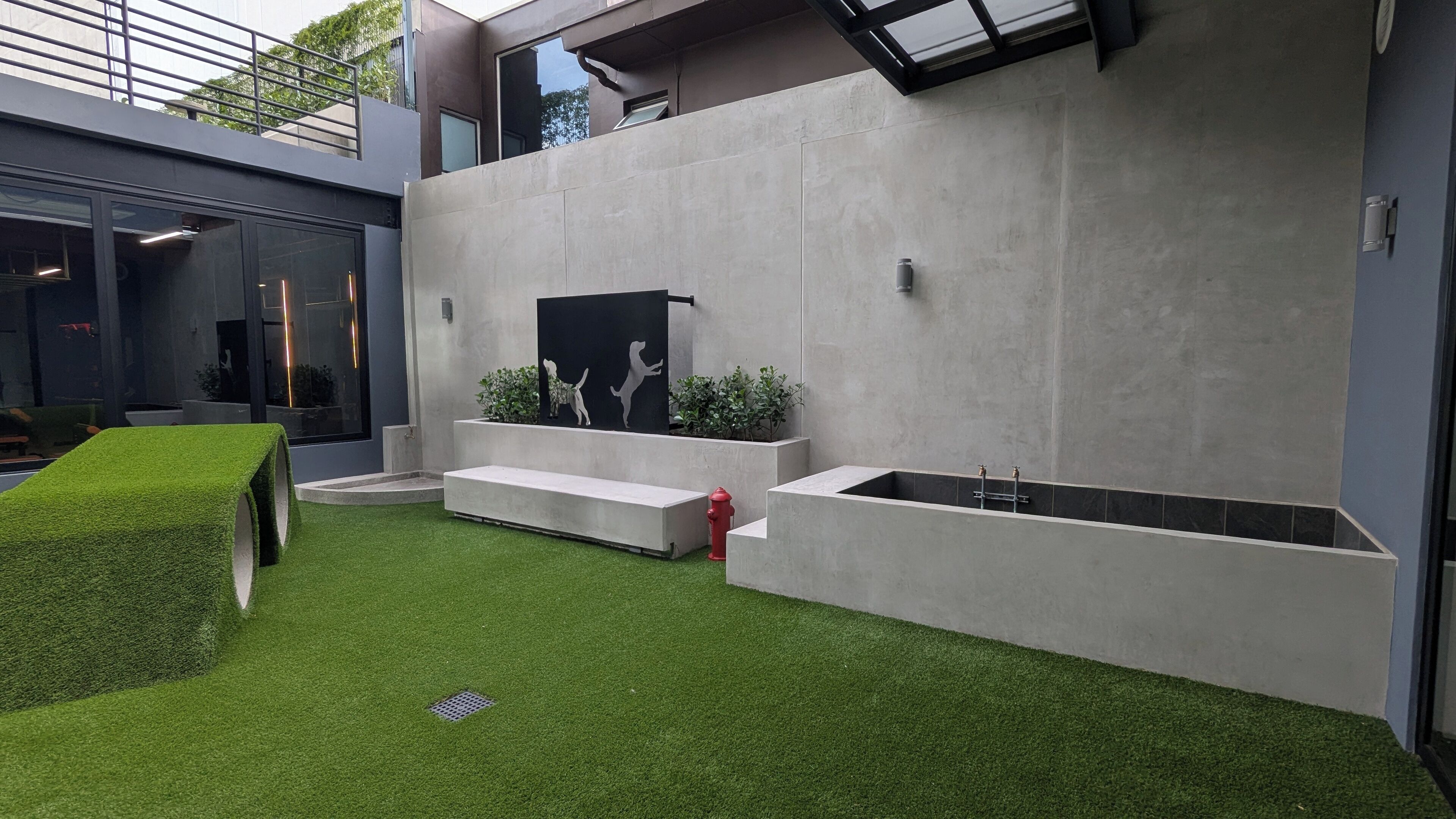 A modern outdoor space with artificial grass, a concrete wall with a black silhouette mural, and a red fire hydrant.