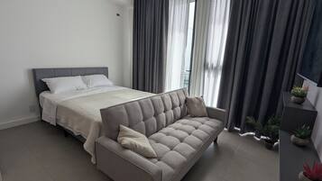 A modern bedroom with a bed, a sofa, and a small desk with plants.