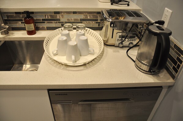 A kitchen counter with a toaster, a kettle, and a plate with white mugs.