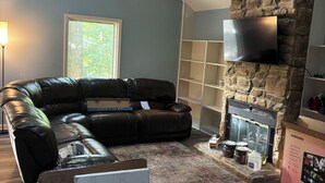 A modern living room with a sectional sofa, a fireplace, a ceiling fan, and a TV mounted on a stone wall.