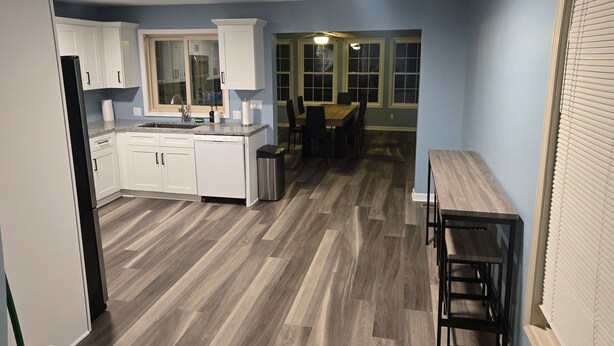 A modern kitchen with white cabinets, a granite countertop, and a dining area with a wooden table and chairs.