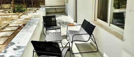 Un patio techado al aire libre con zona de estar, que incluye una mesa y sillas, y una ventana con persianas.