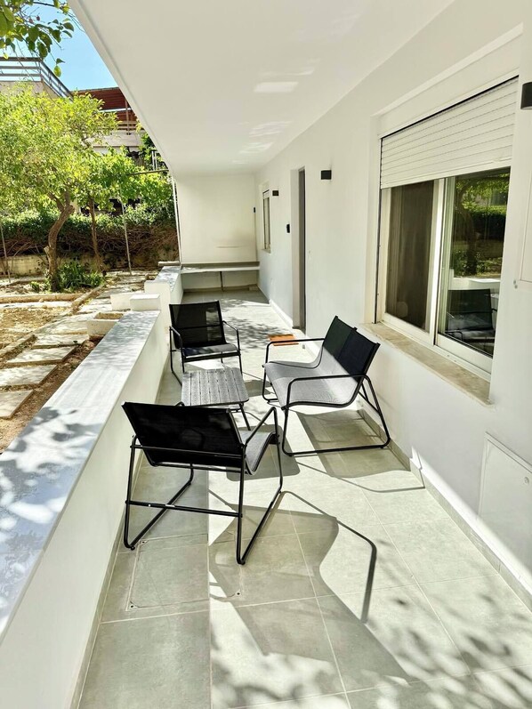 A covered outdoor patio with a seating area, including a table and chairs, and a window with blinds.