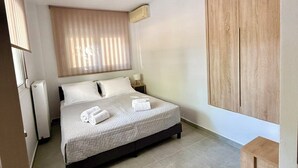 A modern bedroom with a large bed, a wooden wardrobe, a bedside table, and a window with blinds.
