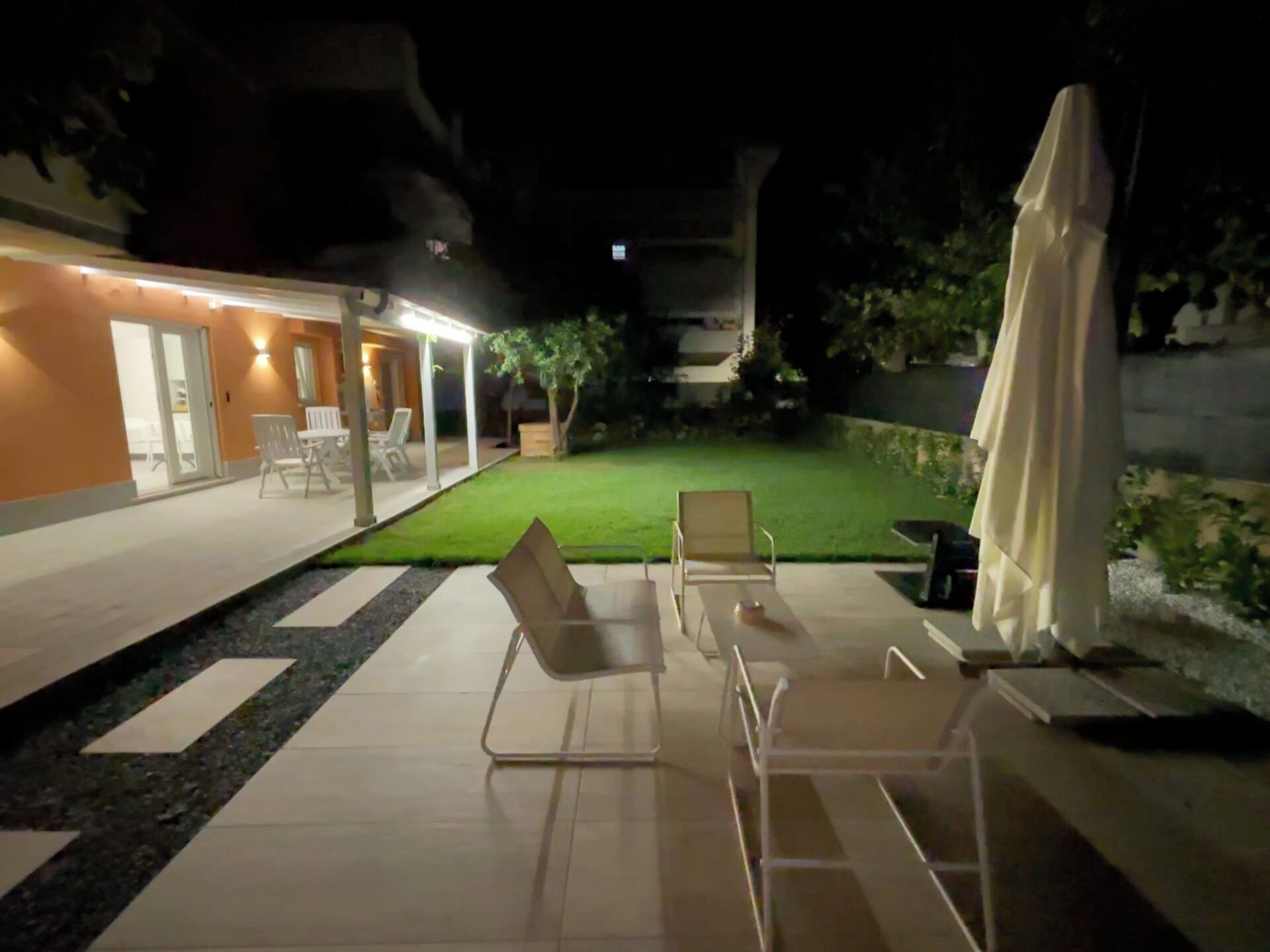 Un espace patio avec des sièges extérieurs, une pelouse et un bâtiment dont les fenêtres sont illuminées.