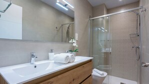 Un baño moderno con un lavamanos grande de color blanco, una cabina de ducha con paredes de cristal y un mueble de tocador de madera.