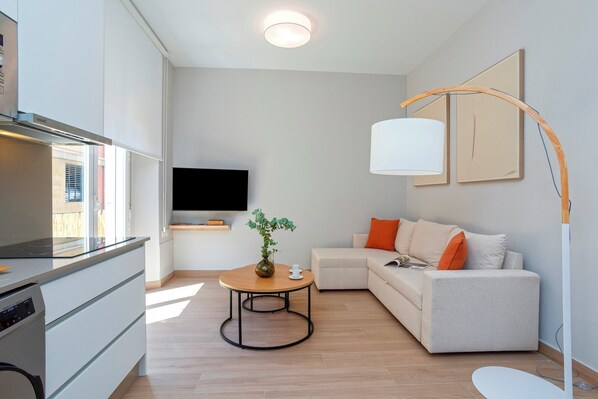 Una sala moderna con un sofá, una mesa de centro con una planta, un televisor de pantalla plana y una zona de cocina con estufa.