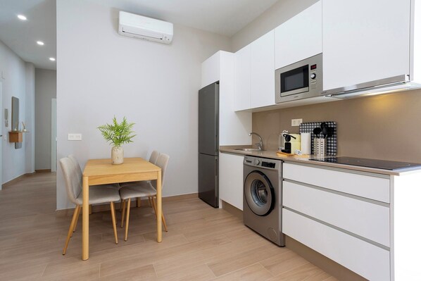 Una cocina moderna con lavadora, microondas y refrigerador. Hay una mesa de comedor con sillas y una planta en maceta.