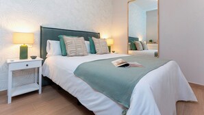 Een keurig opgemaakte slaapkamer met een groot bed, twee nachtkastjes met lampen, een spiegel en behang met een patroon.