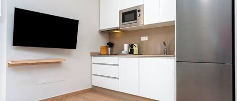 Una cocina moderna con televisor de pantalla plana en la pared, refrigerador de acero inoxidable y microondas.