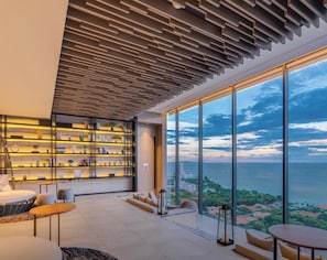 A modern interior with a large window overlooking a coastal view, a built-in bookshelf, and a seating area. - Stunning Sea View On High Floor (Pattaya)