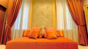 Un letto grande con biancheria arancione e molti cuscini, affiancato da tende rosse e un muro decorato.