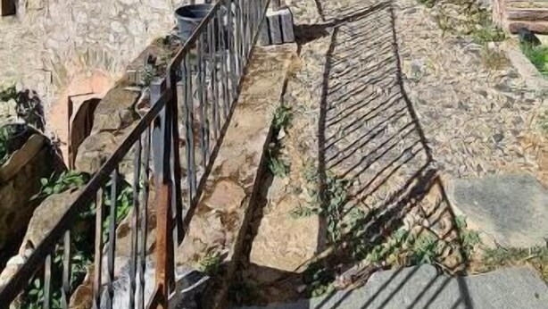 Un sendero de piedra que conduce a una entrada abovedada de un edificio con una pared de piedra rústica.
