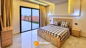 A modern bedroom with a large bed, a nightstand, a wooden dresser, and a sliding glass door leading to a balcony. - Villa with pool Aghmat (Marrakesh)