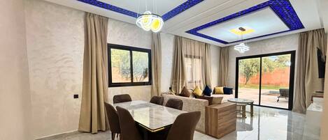 A spacious living area with a dining table, sofas, and a large window.