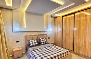Une chambre à coucher comprenant un lit, des tables de chevet, une armoire et un éclairage intégré.