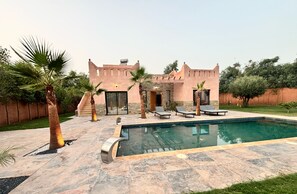 Une maison avec une piscine, des palmiers et une terrasse en pierre.