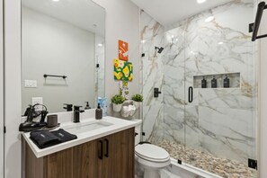 Un baño moderno con pared de ducha de mármol, tocador con lavamanos y retrete.
