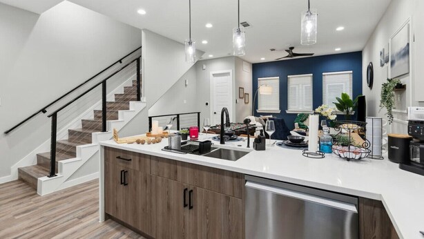 A modern kitchen with a central island, stainless steel dishwasher, and pendant lighting.