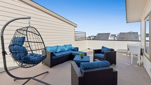 Une terrasse sur le toit, aménagée avec du mobilier d’extérieur, notamment un fauteuil suspendu, des canapés et une table.