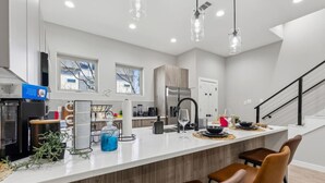 Une cuisine moderne dotée d’un îlot central, d’appareils électroménagers en acier inoxydable et de luminaires suspendus.