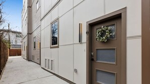 Un bâtiment moderne à la façade beige, avec une porte marron ornée d’une guirlande et un trottoir étroit.