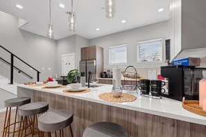 A modern kitchen with a central island, bar stools, and a coffee station. - The Jasper 2BD TH: 7ST Walkable, Stylish & Homey! (Fort Worth)